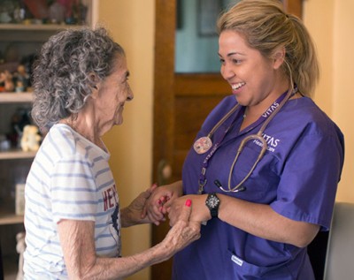 A VITAS nurse and patient hold hands and smile